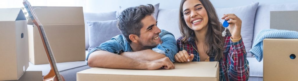 Woman and man surrounded by moving boxes smiling in their new home